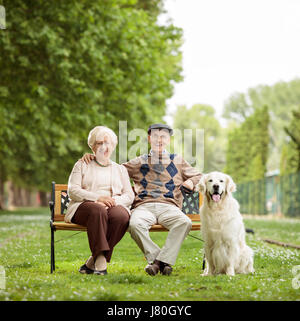 Vieux couple heureux avec un chien assis sur un banc dans le parc Banque D'Images