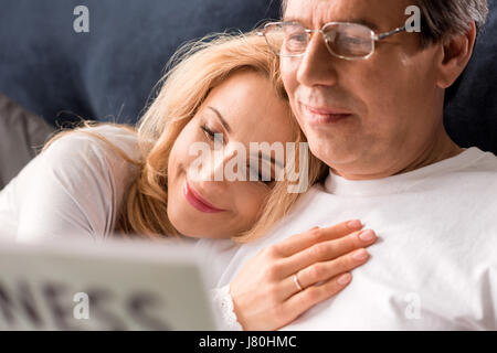 Heureux couple sitting on bed, Man reading newspaper at home Banque D'Images
