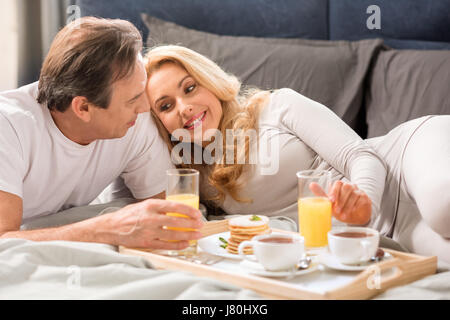 Heureux couple d'âge moyen ayant le petit déjeuner ensemble au lit Banque D'Images