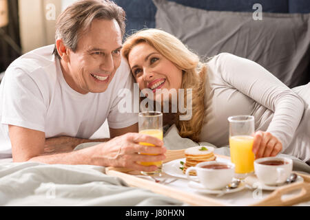 Heureux couple d'âge moyen ayant le petit déjeuner ensemble au lit Banque D'Images