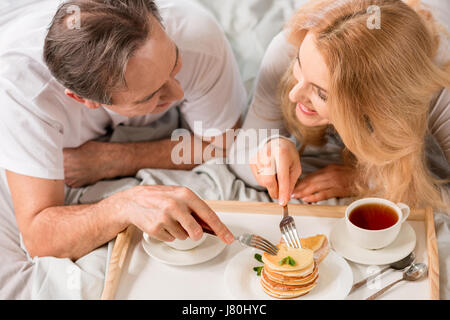 Heureux couple d'âge moyen ayant le petit déjeuner ensemble au lit Banque D'Images