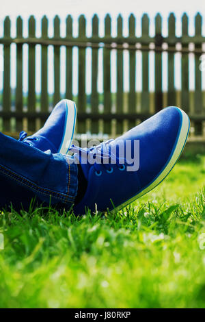 Les pieds mâles en bleu chaussures de jeter sur une herbe verte fraîche dans l'arrière-cour. Se reposant dans un beau jour d'été. Banque D'Images