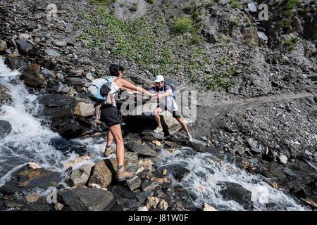 Jeune homme aidant une femme traversant un petit ruisseau de montagne, à l'Alpes, France Banque D'Images