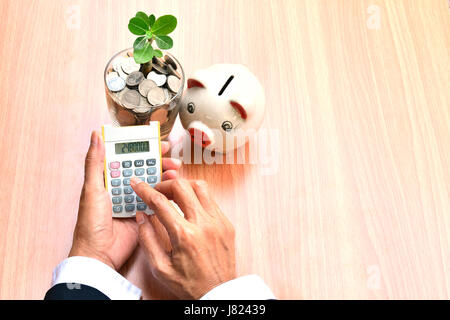 Finances, de la main de personne utilisant calculatrice avec des pièces en verre et white piggy bank Banque D'Images