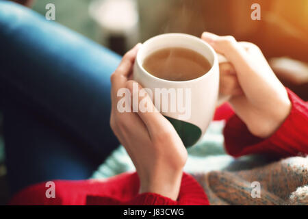 Close up of Pretty woman's hands holding pull rouge tasse de thé dans la lumière du soleil du matin. Banque D'Images