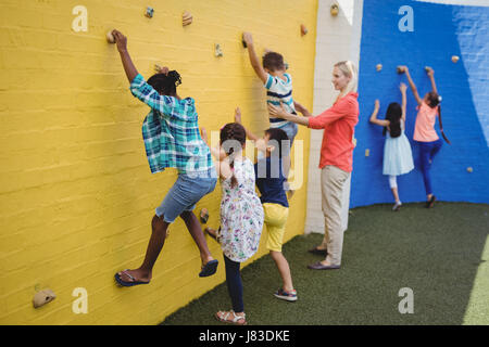 Aider les enfants en formateur mur d'escalade à l'école Banque D'Images