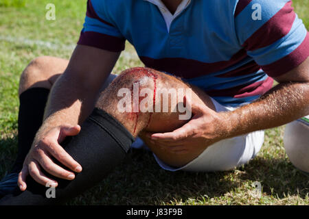 Section intermédiaire de joueur de rugby avec genou blessé assis sur terrain Banque D'Images