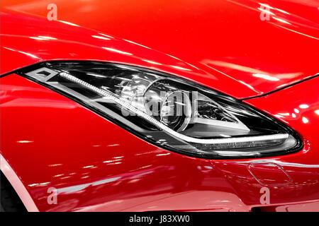 Gros plan du phare de voiture dans la nuit. Les feux avant de la voiture sport rouge. La lumière de la voiture. Banque D'Images