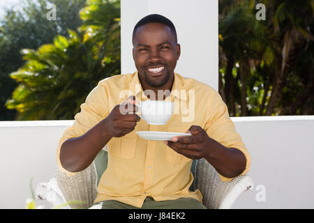 Portrait of smiling young man holding Coffee cup alors qu'il était assis au café Banque D'Images