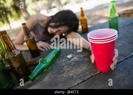 Femme ivre dormir sur la table et la tenue d'un verre de bière dans le parc Banque D'Images