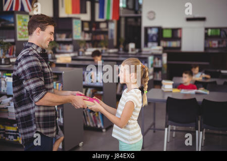 Heureux professeur donnerait livre à girl in library à l'école Banque D'Images