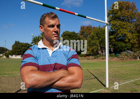 Joueur de rugby réfléchie avec les bras croisés debout à conditions égales aux beaux jours Banque D'Images