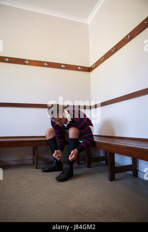 Rugby player lier tout en sportsashoes assis sur un banc dans le vestiaire Banque D'Images