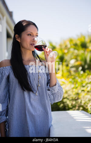 Young woman drinking red wine en position debout en balcon au restaurant Banque D'Images