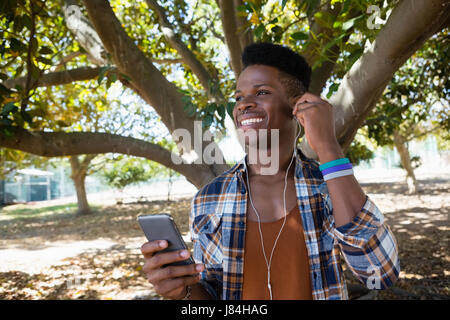 Jeune homme avec vos écouteurs à écouter de la musique sur téléphone mobile dans le parc Banque D'Images