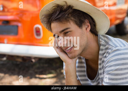 Thoughtful homme assis dans le parc avec le camping-car en arrière-plan Banque D'Images