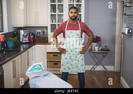 Portrait of young man wearing apron en position debout avec les mains sur la hanche dans la cuisine Banque D'Images