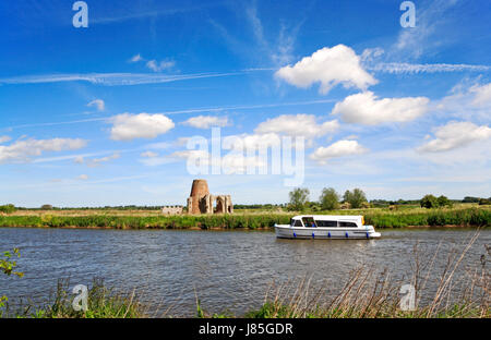 Un bateau sur la rivière Bure dans les Norfolk Broads National Park à propos de passer St Benet's Abbey Mill de drainage et de gardien des ruines. Banque D'Images