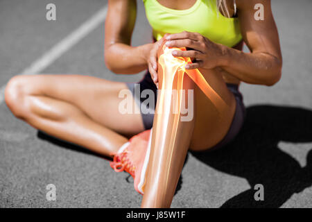 La section basse de la sportive souffrant de douleur au genou alors qu'il était assis sur la voie au cours de journée ensoleillée Banque D'Images