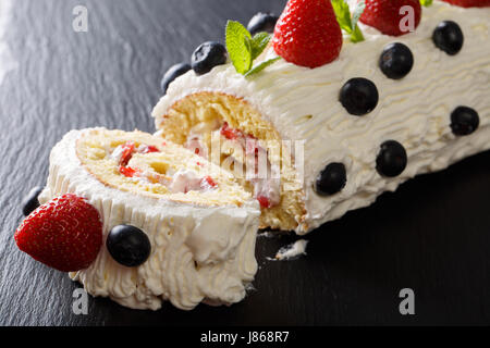 Couper le rouleau de fraises avec de la crème fouettée, de menthe et de bleuets close-up sur la table horizontale. Banque D'Images