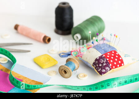 Outils de couture, patchwork, la couture et de la mode concept - close-up sur blanc 24 avec des ciseaux, des gants, des morceaux de tissu patchwork coloré, de savon, de mesure, compteurs thread spools, boutons. Banque D'Images