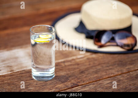 Deux tranches de citron dans un verre d'eau avec un chapeau et des lunettes de soleil dans l'arrière-plan Banque D'Images