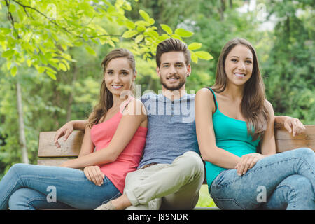 Les adolescents souriants se détendre à la park pendant un jour d'été, ils sont assis sur un banc en bois et looking at camera Banque D'Images