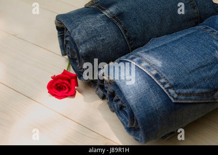 Jean bleu plié avec rose rouge sur table en bois et sur fond de bois. Banque D'Images