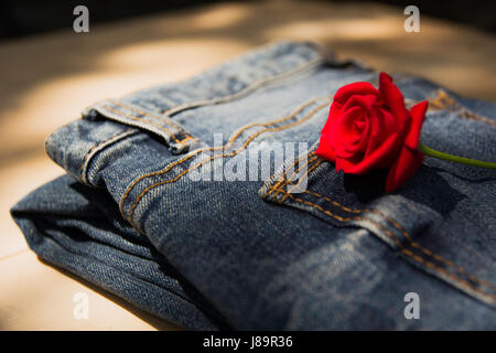 Jean bleu plié avec rose rouge sur table en bois et sur fond de bois. Banque D'Images