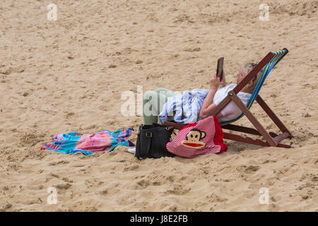 Bournemouth, Dorset, UK. 28 mai, 2017. UK : Météo des plages de Bournemouth à temps couvert, mais le soleil essaie de percer. Les visiteurs vers le bord de la tête pour tirer le meilleur de la Banque week-end de vacances. Femme assise dans une chaise longue à la lecture de livre Kindle. Credit : Carolyn Jenkins/Alamy Live News Banque D'Images