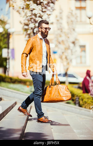 Jeune homme barbu à lunettes avec un sac de voyage qui pose dans les escaliers en ville rue Banque D'Images
