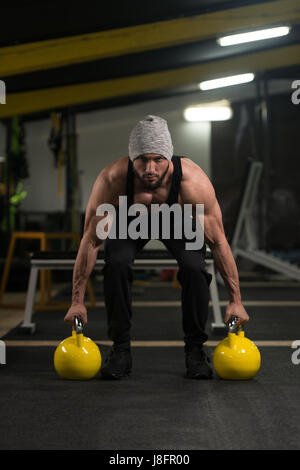 Jeune homme l'élaboration avec électrique Bell dans une sombre salle de sport - le carrossier faisant de l'exercice avec poids lourd Électrique-bell Banque D'Images