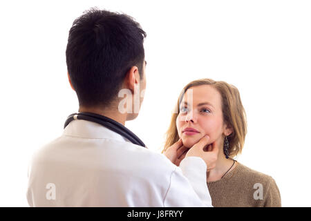 Jeune médecin aux cheveux noirs en robe blanche avec stéthoscope sur son cou examen jeune belle femme avec de longs cheveux bruns en pull et jeans sur whi Banque D'Images