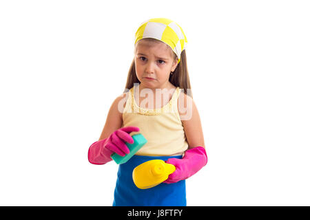 Triste petite fille avec de longs cheveux châtains en chemise jaune et bleu avec des gants et tablier rose jaune foulard vert et jaune éponge holding sur bouteille Banque D'Images