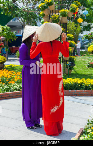 Ho Chi Minh Ville, Vietnam - Février 07, 2016 : Deux jeunes femmes vietnamiennes en robe traditionnelle Ao Dai se font passer pour des images en face de fleurs à Banque D'Images