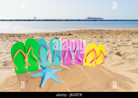 Été plage fun - jeu de famille sandales - vert, bleu, rose et jaune - dans le sable sur la plage de Las Teresitas, Tenerife, Canarias Banque D'Images