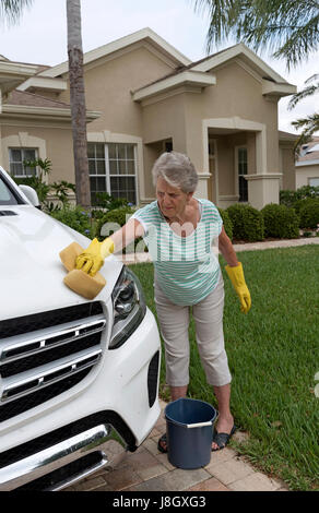 Femme âgée laver une voiture sur l'allée d'une maison en Amérique. Banque D'Images