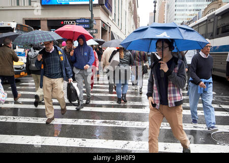 Les gens des parasols traverser une rue de ville humide pendant la pluie douche Midtown New York City USA Banque D'Images