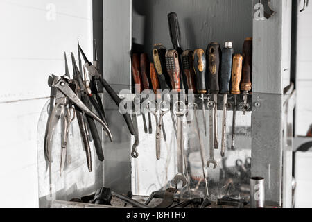 Assortiment de faire vous-même des outils de travail suspendue dans un placard contre un mur de l'huile moteur sale. Banque D'Images