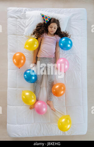 Rêves heureux. Petite belle fille portant un chapeau d'anniversaire et d'avoir un parti tout en étant entouré par des ballons colorés Banque D'Images