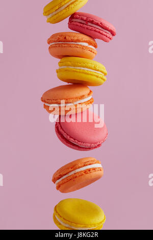 Différents types de macarons dans motion relevant sur fond rose. Doux et coloré qui tombent ou qui volent les macarons français en mouvement. Banque D'Images