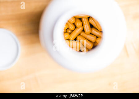plat de capsules curcuma dans une bouteille en plastique blanc sur une table en bois Banque D'Images