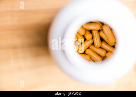 plat de capsules curcuma dans une bouteille en plastique blanc sur une table en bois Banque D'Images