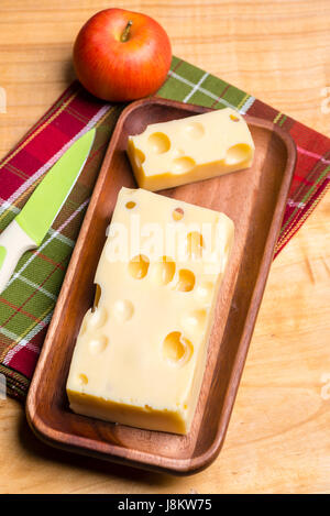 Un morceau de fromage suisse emmethal sur une plaque en bois, rustique un couteau vert et une fraîche appe. Banque D'Images