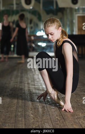 Belle jeune blonde woman sitting on her foot exercices au ballet school. Groupe de danseurs de ballet trouble debout dans l'arrière-plan Banque D'Images