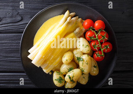 Les asperges blanches avec sauce hollandaise et pommes de terre nouvelles close-up sur une plaque horizontale vue du dessus. Banque D'Images