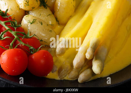 La vitamine alimentation : les asperges avec sauce hollandaise, pommes de terre nouvelles, verts et tomates close up sur la plaque noire horizontale. Banque D'Images