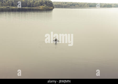 L'exploration de l'homme dans le bateau au milieu de vastes étendues de lac paisible. Symbolisant la solitude et la recherche Banque D'Images