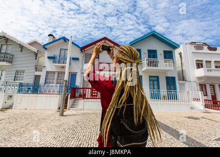 Young woman taking photo touristique sur maisons à rayures téléphone au Costa Nova, Portugal. Girl dreadlocks photographies bâtiments colorés. Banque D'Images