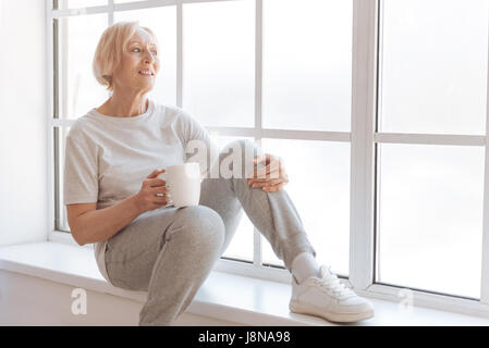 Minute de détente. ont La sportive énigmatique assis sur le rebord de la tasse blanche en main droite tout en mettant la main gauche sur le genou gauche Banque D'Images